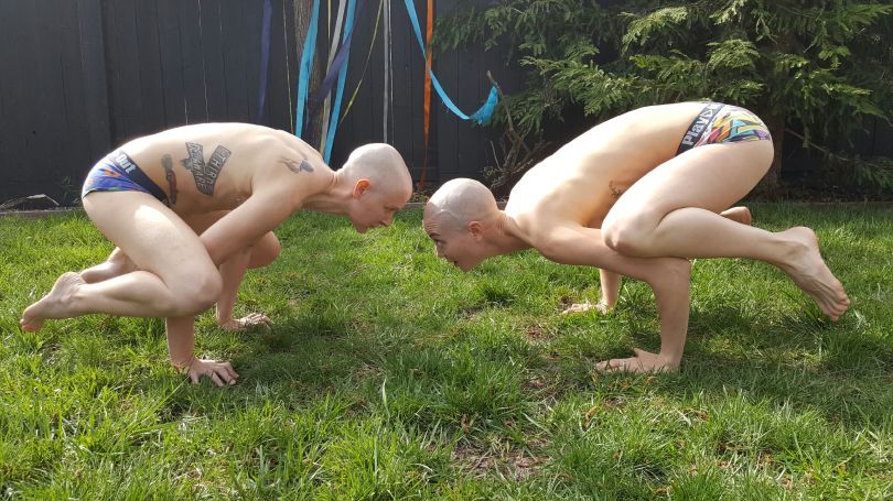 Image is of two white people with freshly shaved heads balancing on their hands when knees propped on their elbows.