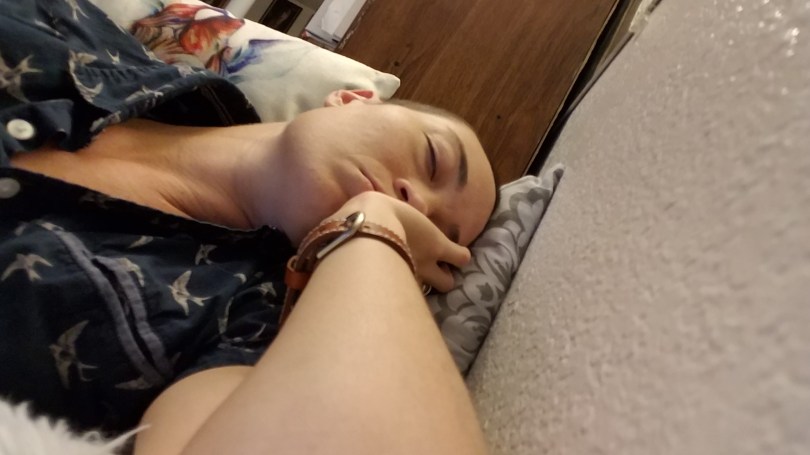 a picture of a white person's (me) chest, head, and forearm. My head is sideways against a pillow and my cheek and lower half of my face are resting against my hand. My eyes are closed